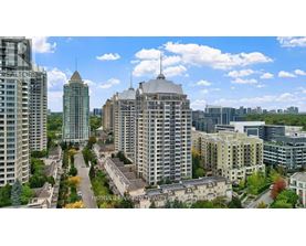 A cityscape with a mix of modern and older buildings, a clear sky, and a road with trees on the side.