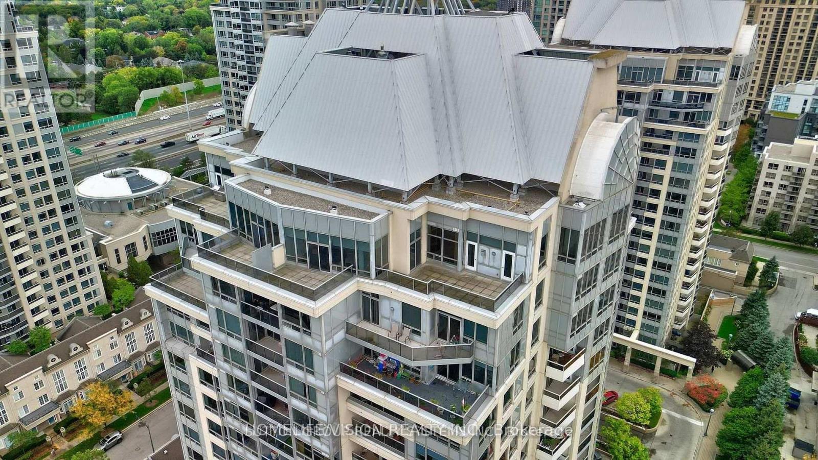 A modern building with a grey roof is surrounded by other buildings.