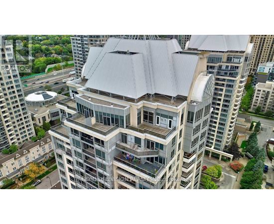 A modern building with a grey roof is surrounded by other buildings.