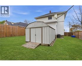 A shed with a white exterior and a brown door is situated in a grassy backyard.