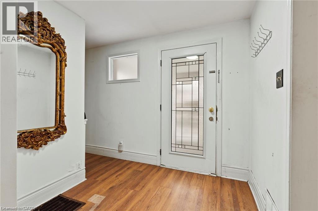A white door with a glass panel and a gold handle is in a room with a wooden floor and a large mirror on the wall.