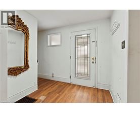 A white door with a glass panel and a gold handle is in a room with a wooden floor and a large mirror on the wall.