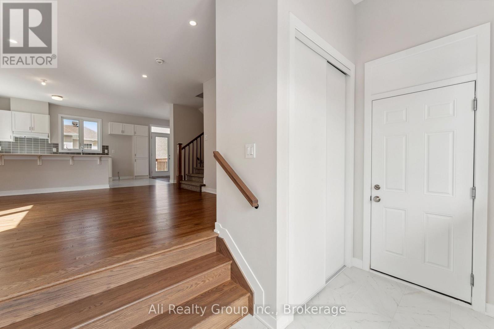 A spacious room with wooden floors and white walls, leading to a staircase.