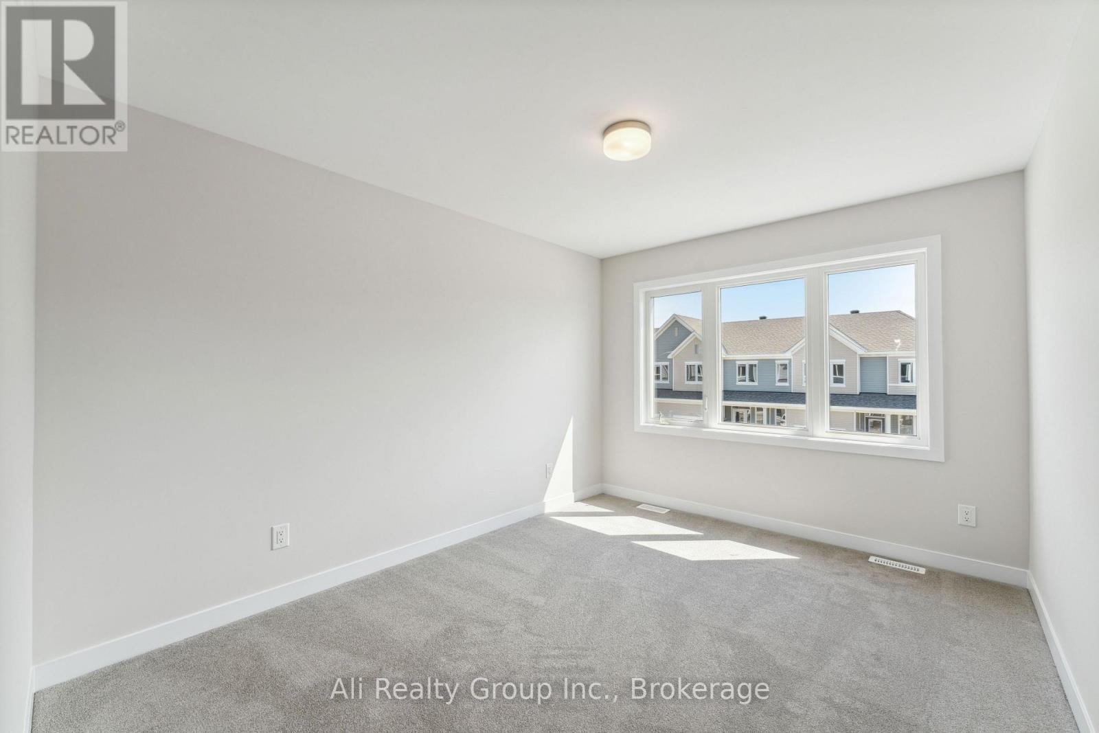 A room with a carpeted floor and a window showing a view of other buildings.