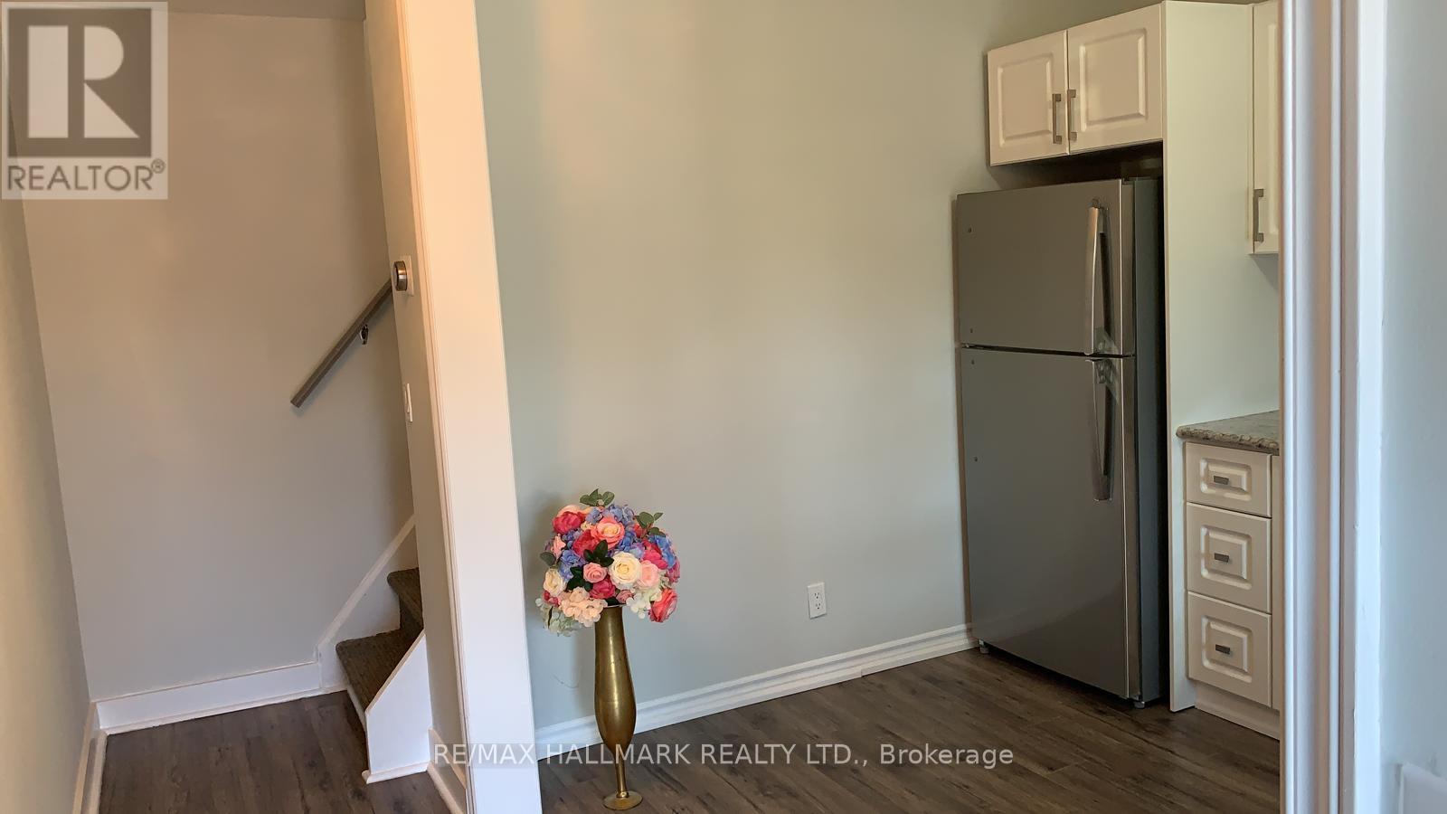 A kitchen with a refrigerator, a flower vase, and a staircase.