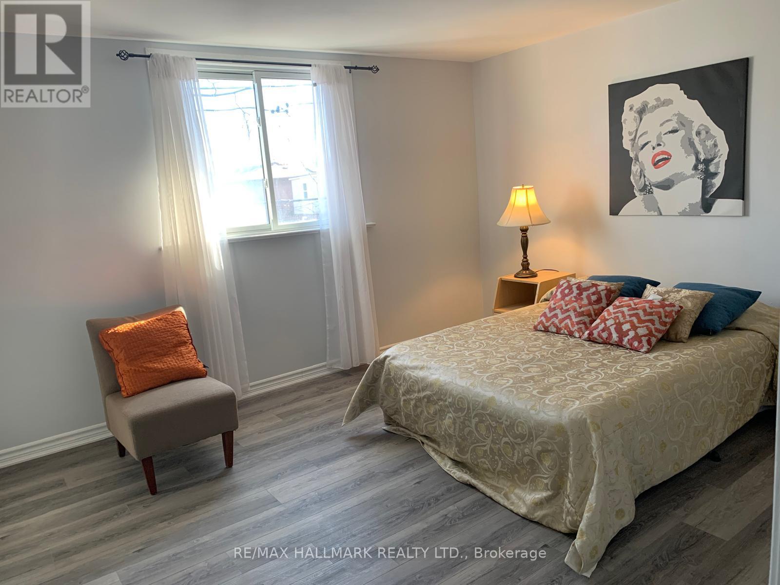 A bedroom with a bed, chair, and a painting of Marilyn Monroe.
