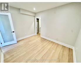 A room with wooden flooring and white walls, with a doorway leading to another room.