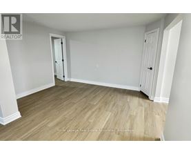 A room with wooden flooring and white walls, with a door on the left and a closet on the right.