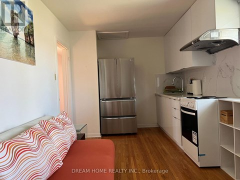 A small kitchen with a refrigerator, oven, and a table with a red cushion on it.
