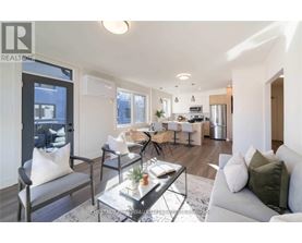 A modern living room with a grey sofa, a glass coffee table, and a dining area in the background.