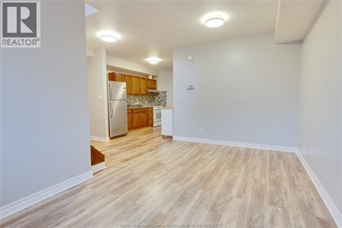 A room with wooden flooring and a kitchen area with a refrigerator and cabinets.