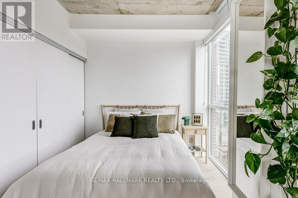 A bedroom with a white bed and a potted plant on the side.