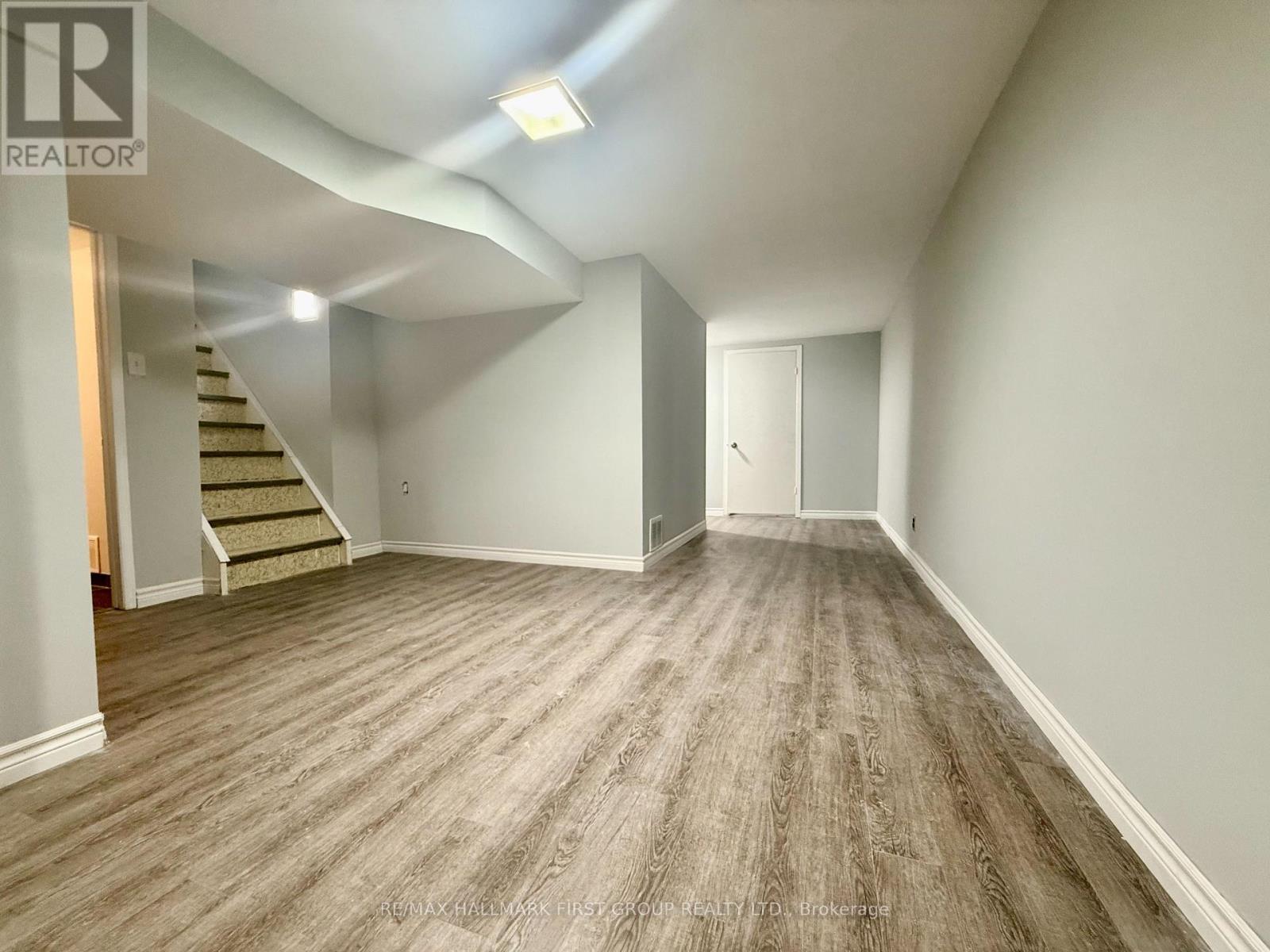 A spacious room with wooden flooring and a staircase leading to another level.