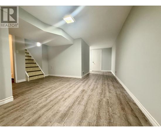 A spacious room with wooden flooring and a staircase leading to another level.