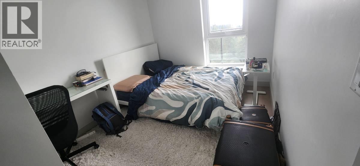 A bedroom with a bed, a chair, a suitcase, and a window.