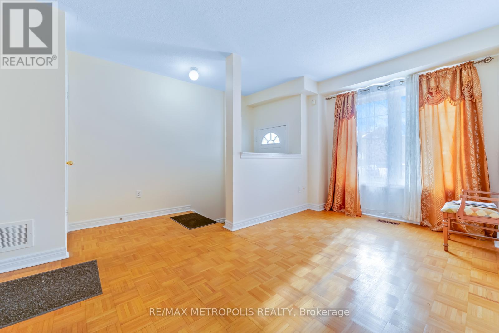 A room with a wooden floor and a window with orange curtains.