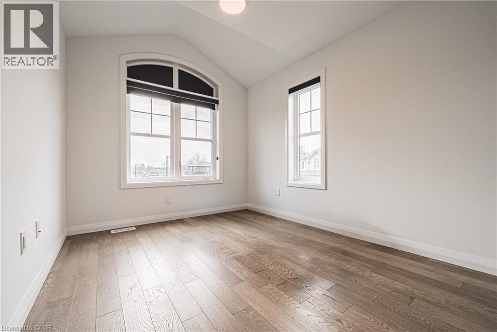 A spacious room with wood flooring and two windows.