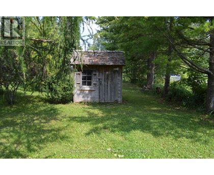 A small wooden shed sits in a grassy area surrounded by trees.