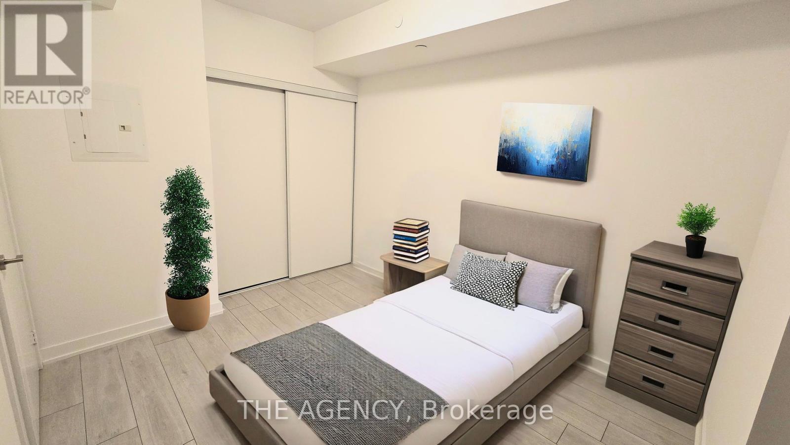 A bedroom with a bed, nightstand, and a plant.