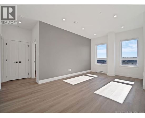 A spacious room with wooden floors and two windows.