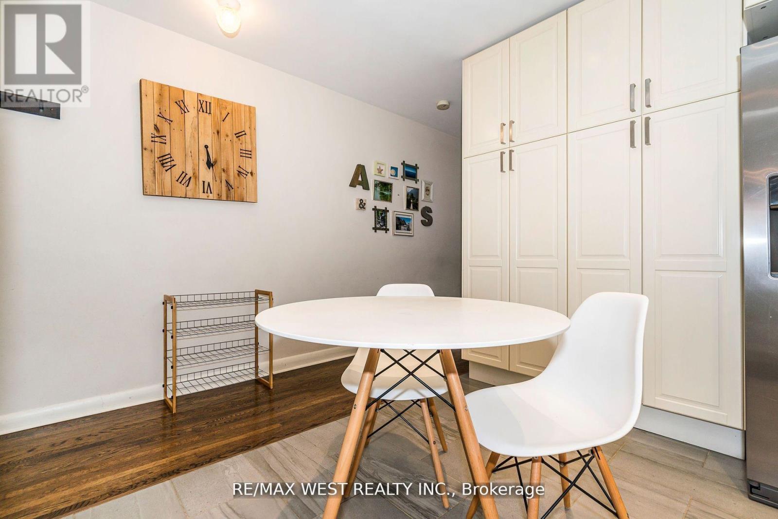 A dining room with a white table and chairs, a wooden clock, and a fridge.