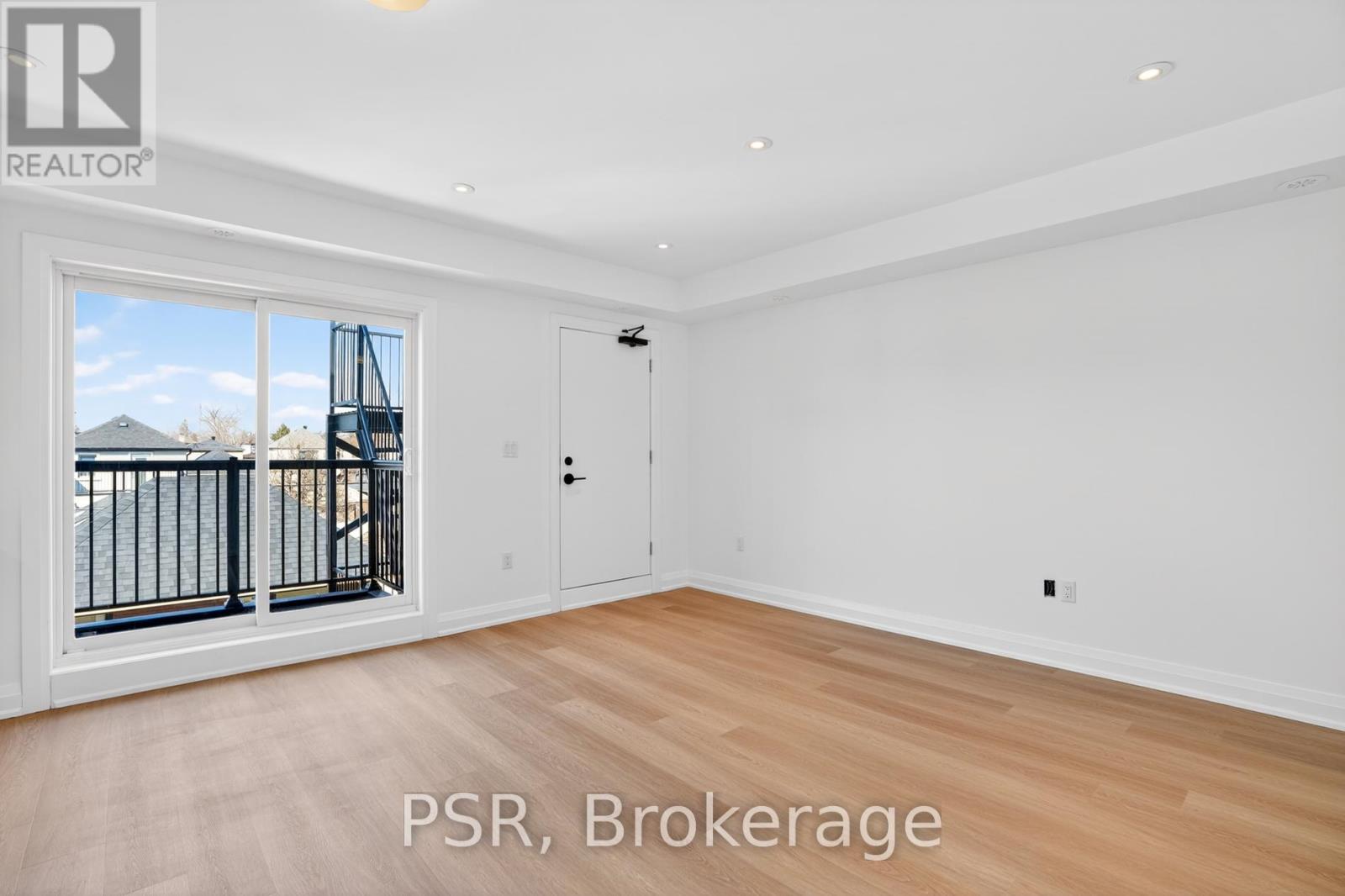 A room with a door leading to a balcony with a view of a house and trees.