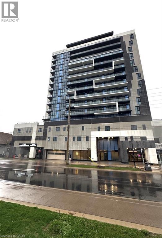 A tall building with a glass facade stands in front of a grey building.
