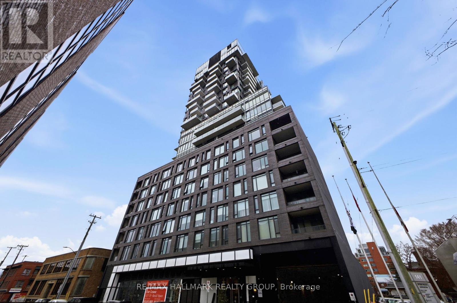 A tall building with a glass facade is under construction with a sign that reads "Hallmark Realty Group, Brokerage".