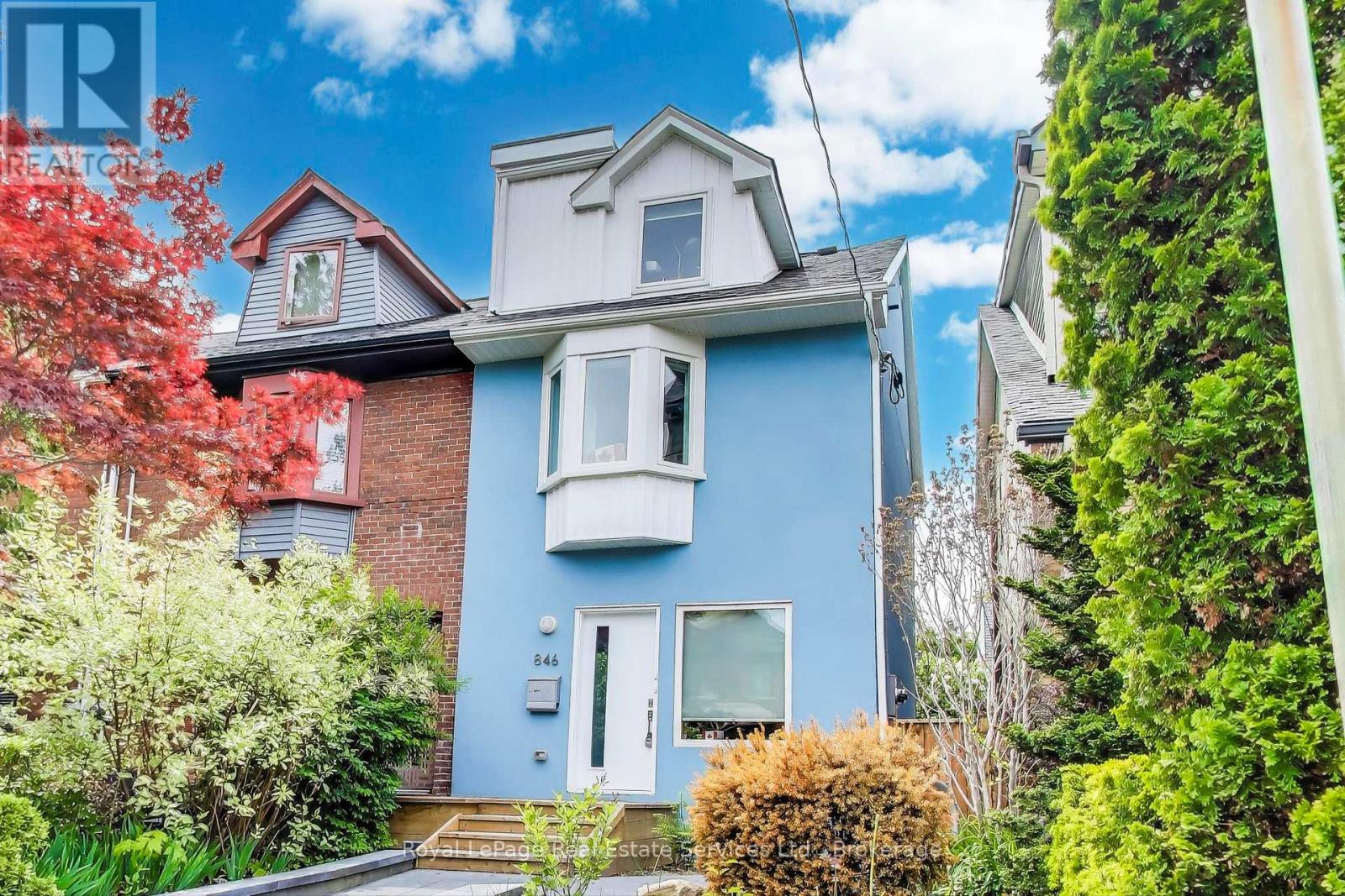 A blue house with a white door and windows surrounded by greenery.