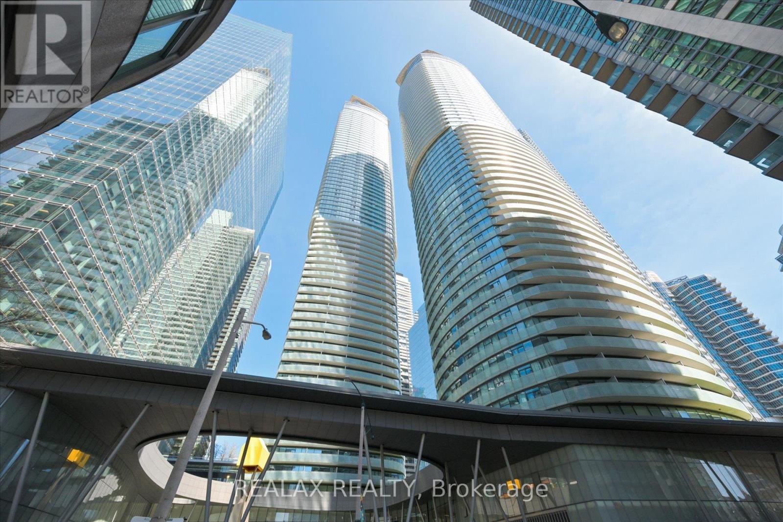 A tall building with a curved glass facade stands in front of two other skyscrapers.