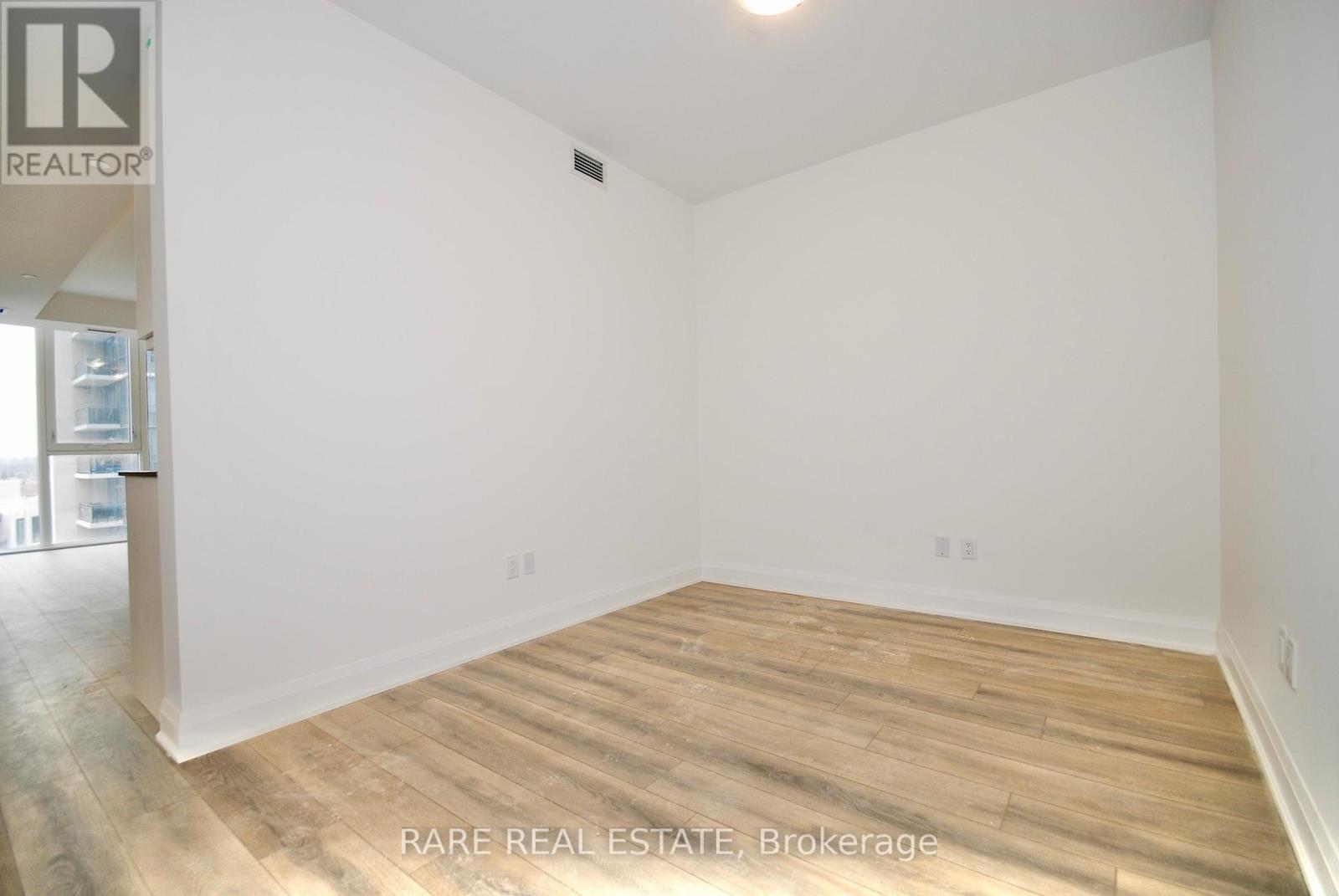 A room with wooden flooring and white walls, labeled as a rare real estate brokerage.