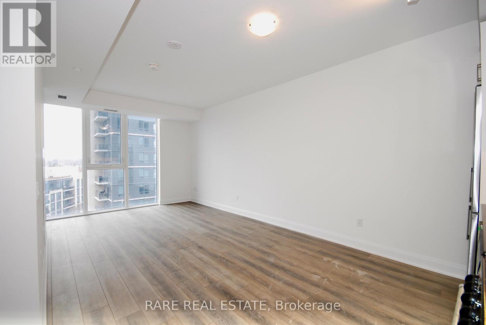 A spacious room with wooden flooring and a large window.