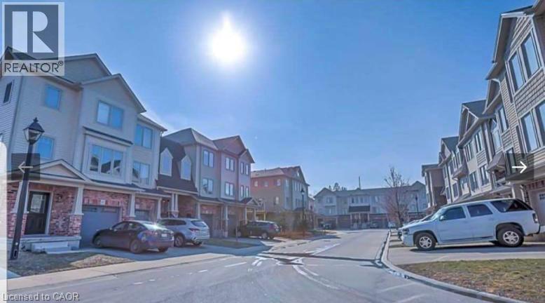 A sunny day in a quiet residential street with houses on both sides and cars parked on the side of the road.