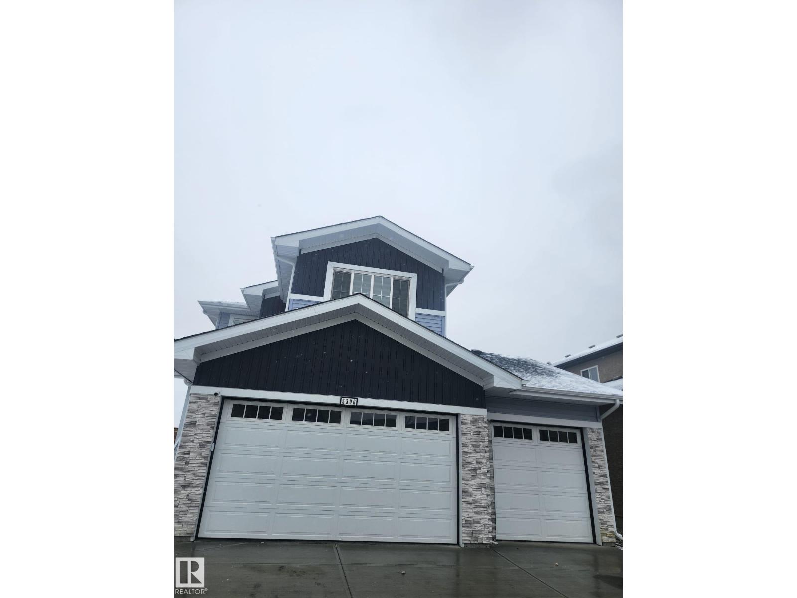 A house with a grey garage door and a stone pillar.