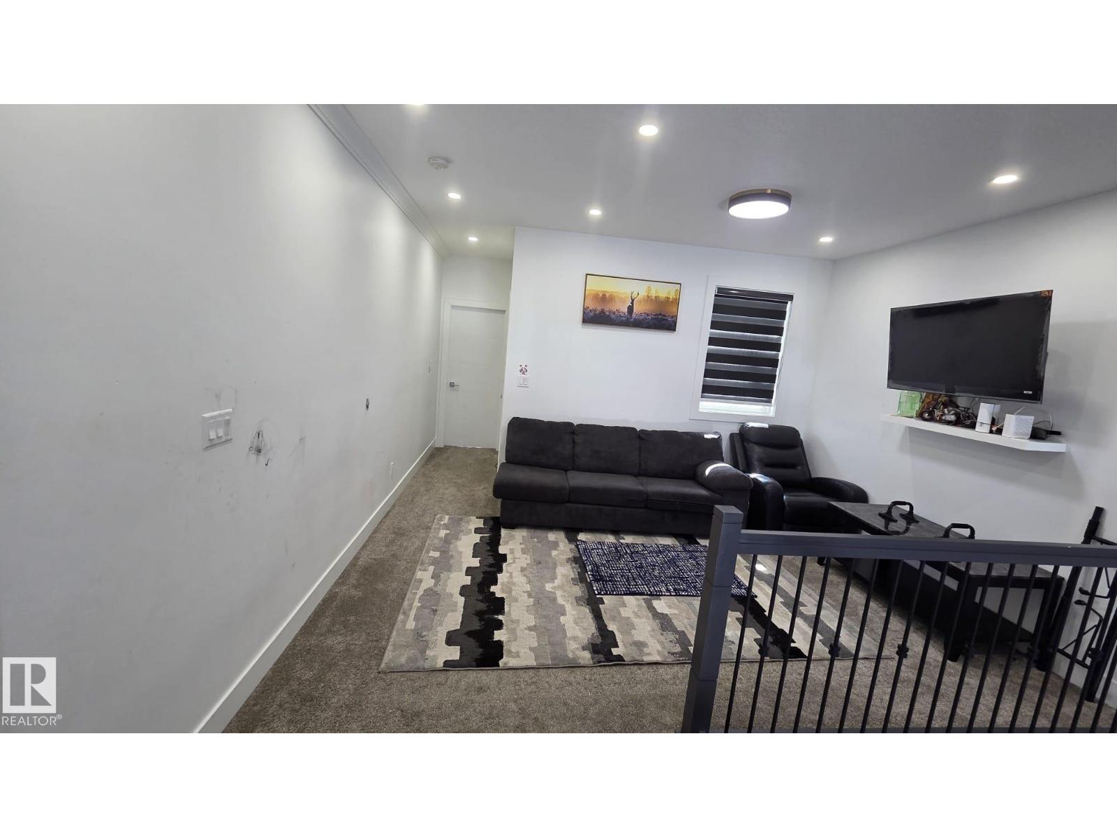 A black couch sits in a living room with a television on the wall.