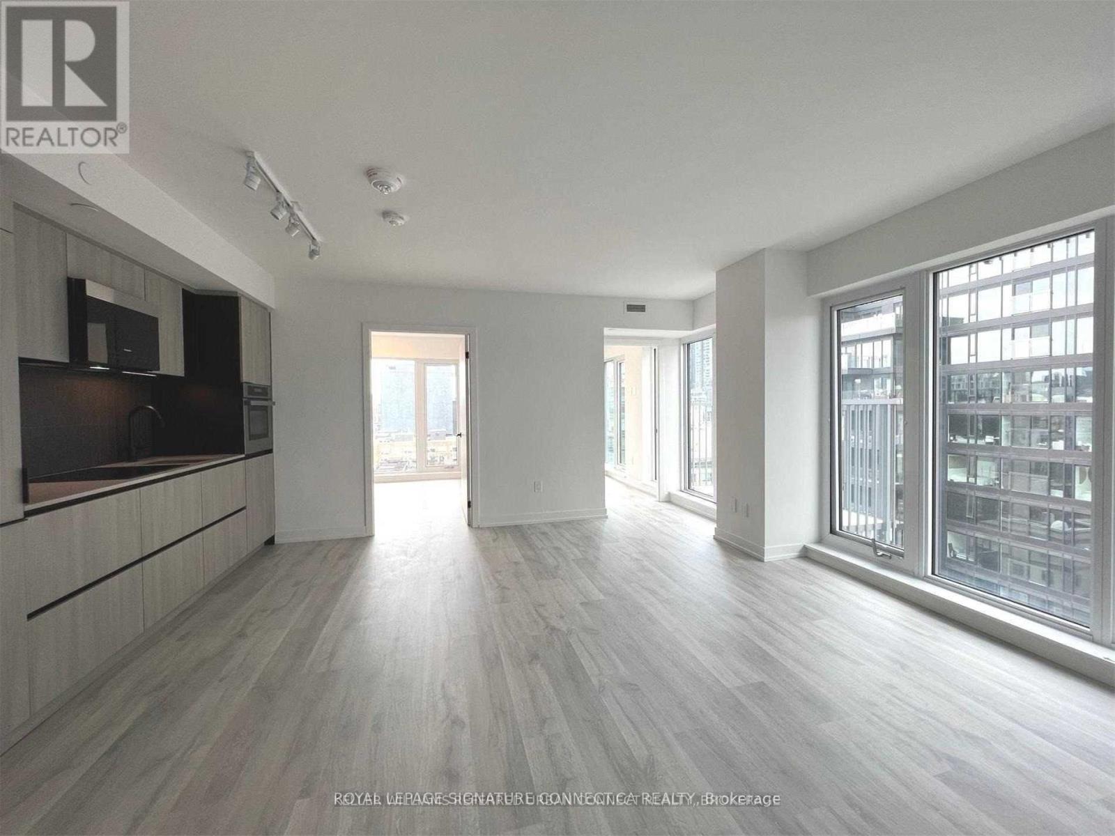 A spacious room with wooden flooring and large windows.
