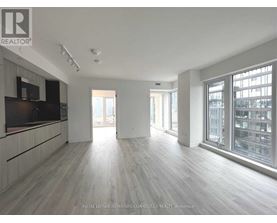 A spacious room with wooden flooring and large windows.