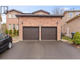 A black car is parked in front of a brick house with a brown garage door.