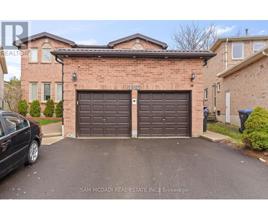 A black car is parked in front of a brick house with a brown garage door.