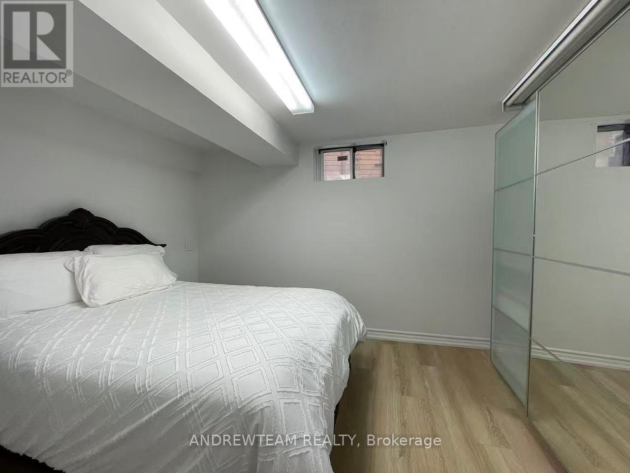 A bedroom with a bed, wooden floor, and a glass walled closet.