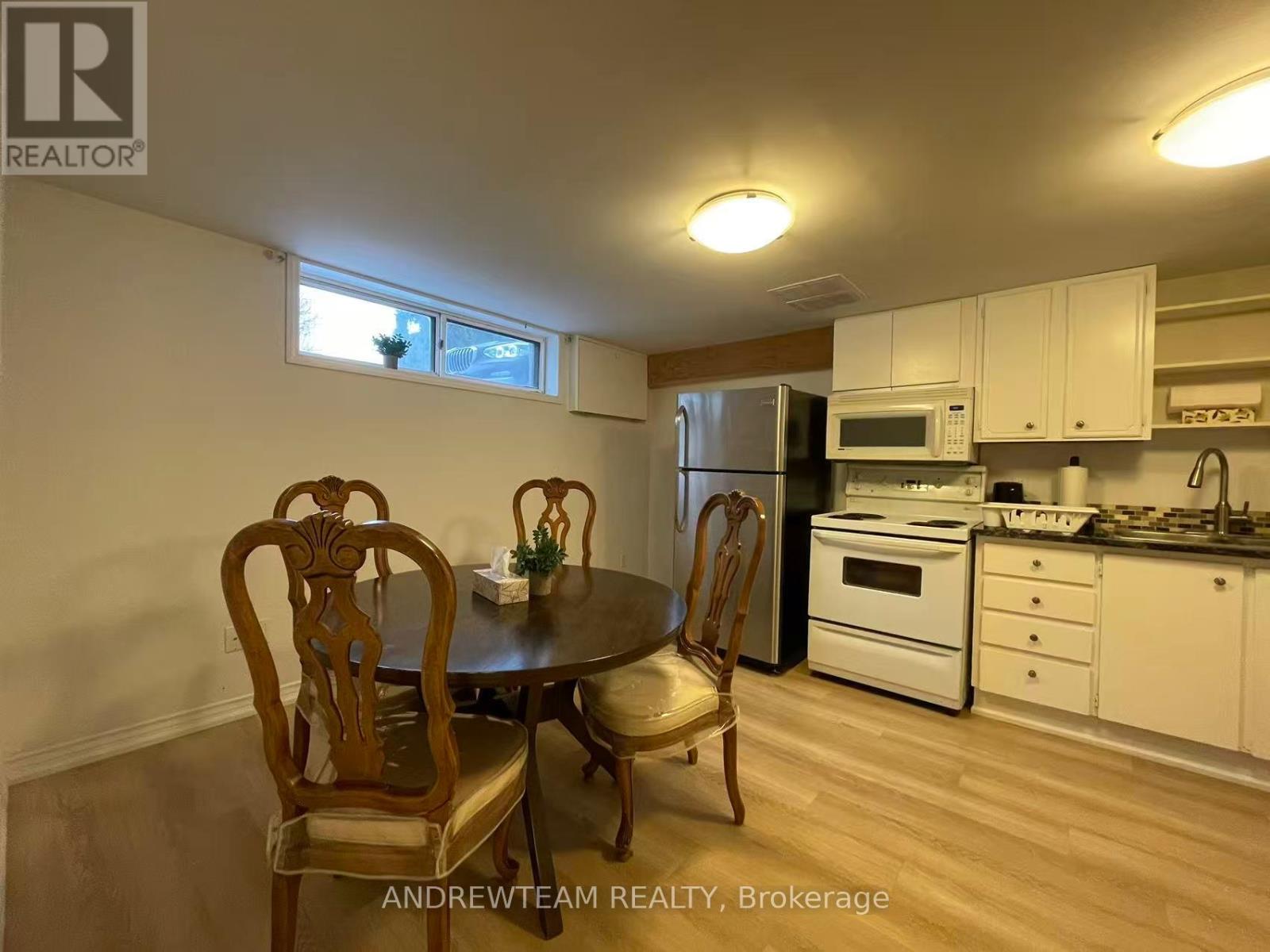 A kitchen with a table and chairs in the foreground and a refrigerator, microwave, oven, and sink in the background.