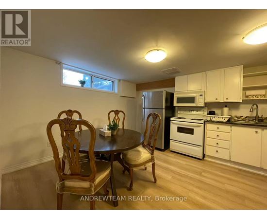 A kitchen with a table and chairs in the foreground and a refrigerator, microwave, oven, and sink in the background.
