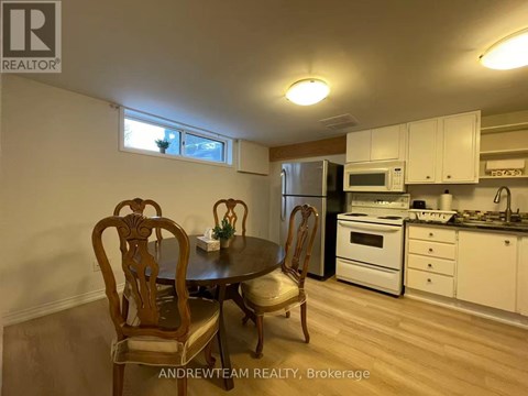 A kitchen with a table and chairs in the foreground and a refrigerator, microwave, oven, and sink in the background.