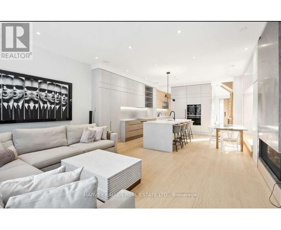 A modern living room with a large painting on the wall and a dining area in the background.