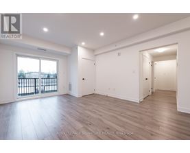 A spacious room with wooden flooring and white walls, with a balcony visible through the window.