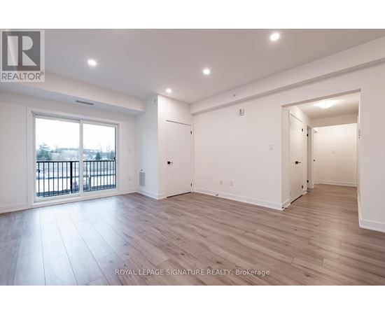 A spacious room with wooden flooring and white walls, with a balcony visible through the window.