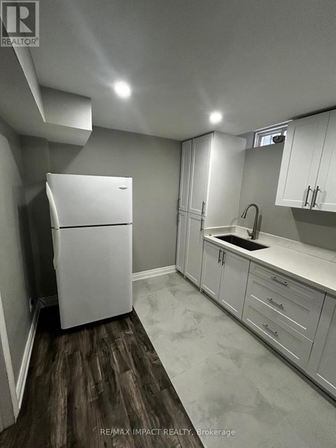 A white refrigerator in a kitchen with white cabinets and a wooden floor.