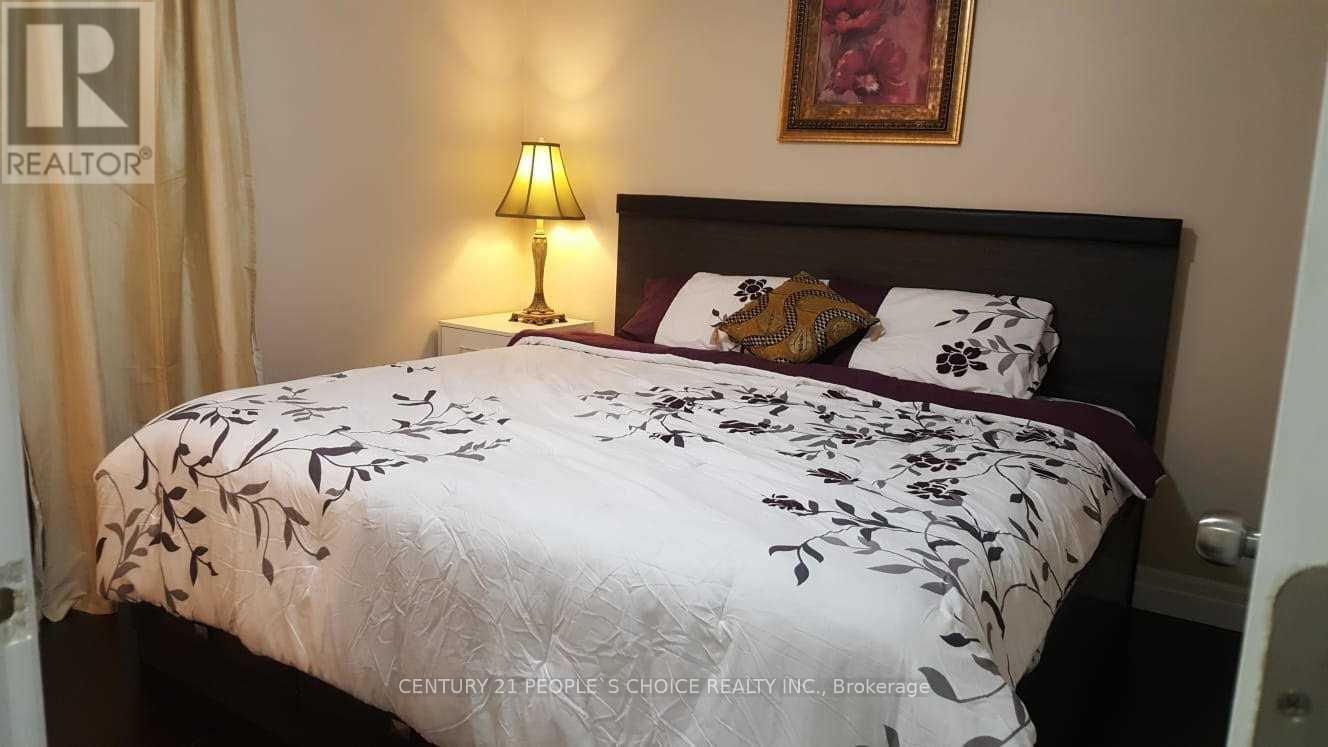 A bed with a floral patterned comforter is in a room with a lamp and a painting on the wall.