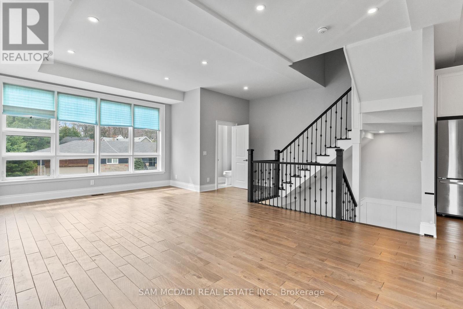 A spacious, well-lit room with a staircase and a view of a residential area outside the window.