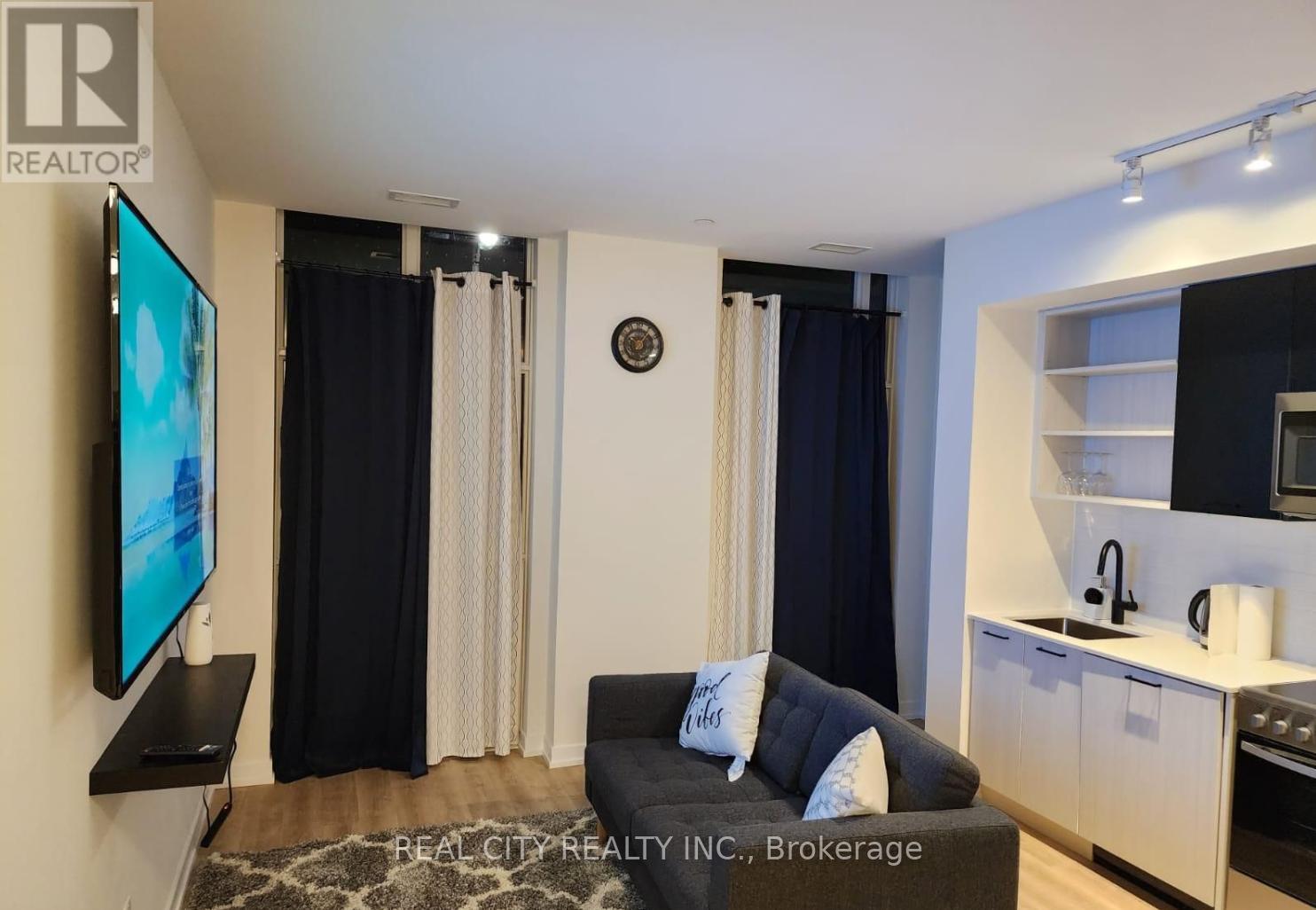 A living room with a couch, television, and kitchen area.